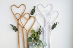 three decorative items are arranged on a white surface with greenery in the shape of hearts