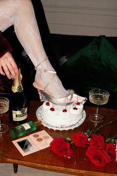 a woman in white stockings and high heels is pouring champagne into a cake with red roses on the table