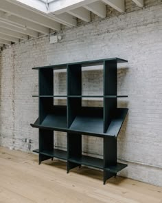 a black shelf sitting on top of a wooden floor next to a white brick wall