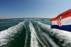 the flag of croatia is flying from a boat in the water with a bridge in the background