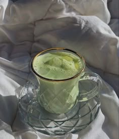 a glass cup filled with liquid sitting on top of a bed covered in white sheets