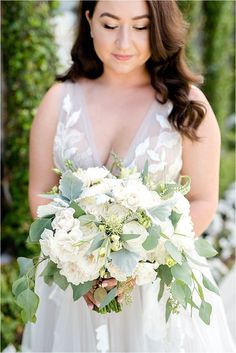 a woman in a wedding dress holding a white bouquet and looking down at her face