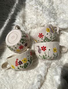 three tea cups and saucers sitting on a white furnishing with flowers painted on them