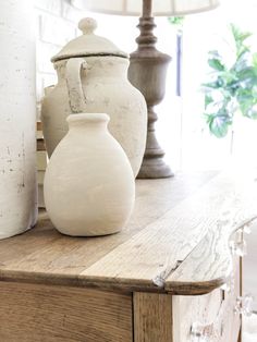 three white vases sitting on top of a wooden table in front of a lamp