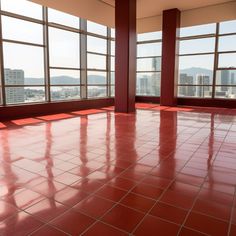 an empty room with red tile floors and large windows looking out on the city skyline