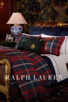 a bed with plaid sheets and pillows in a room next to a lamp on a table