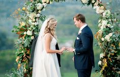 a bride and groom standing in front of an arch with flowers on it at their wedding ceremony