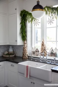 a kitchen decorated for christmas with greenery and decorations on the windowsills, along with white cabinets