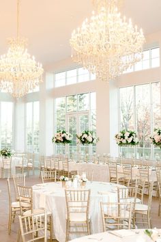 a room filled with lots of tables covered in white cloths and chandeliers