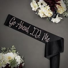 a black sash with the words go ahead it's me on it next to flowers