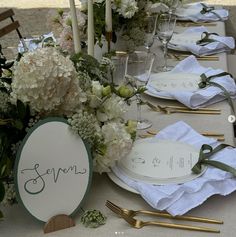 the table is set with white flowers and place settings