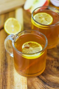 two mugs of tea with lemon slices on the side and apples in the background