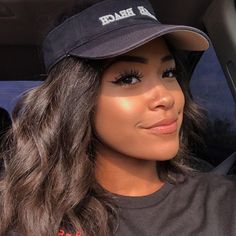 a woman with long hair wearing a black hat and grey t - shirt sitting in the back seat of a car