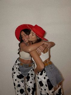 two women in cow print pants and red hats hugging each other with their arms around one another