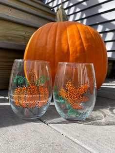 two wine glasses with orange and green designs on them sitting in front of a pumpkin