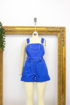 a mannequin wearing blue overalls in front of a gold framed photo frame