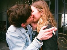 a man and woman kissing each other in front of a gate