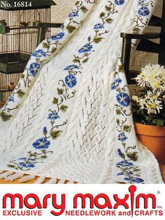 a crocheted blanket with blue flowers on it in front of a birdcage