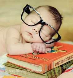 a baby wearing glasses laying on top of a stack of books with his eyes closed