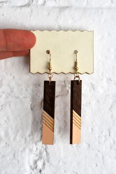 a pair of brown and gold earrings hanging from a hook on a white surface with a person's hand holding it