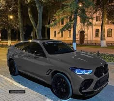 the grey bmw suv is parked on the side of the road at night in front of some trees