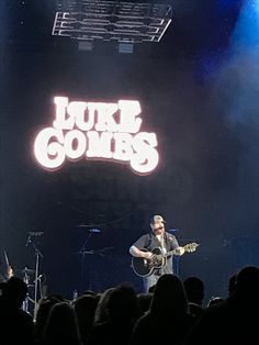 a man playing guitar in front of a crowd on stage with the words luke combs above him