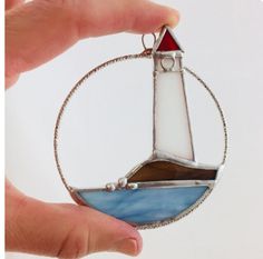 a hand holding a glass ornament with a lighthouse on it