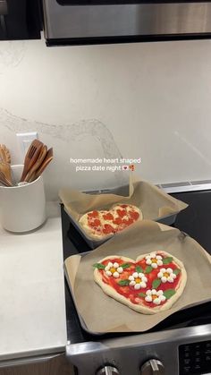 two heart shaped pizzas sitting on top of pans in front of an oven