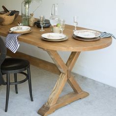 a wooden table with plates and glasses on it next to a black chair in front of a white wall