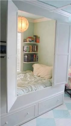 a white bed sitting under a window next to a book shelf