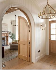 an arched wooden door is open to a living room with white walls and wood floors