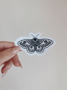 a hand holding up a sticker with a moth on it's back side