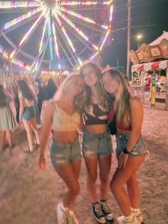 three young women standing next to each other in front of a ferris wheel