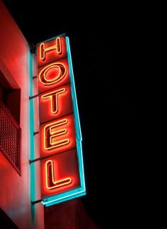 a neon hotel sign on the side of a tall building at night with red and blue lights