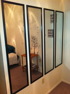 three mirrors on the wall in front of a small table with a vase and tree