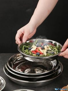 a person holding a bowl with food in it on top of a metal plate next to other dishes