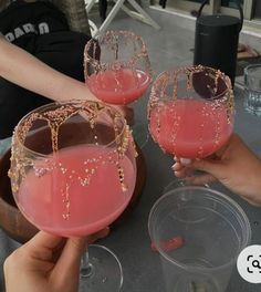 two people holding up wine glasses with pink liquid in them and gold beading on the rim