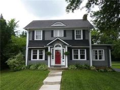 a large gray house with a red front door and white trim on the side of it