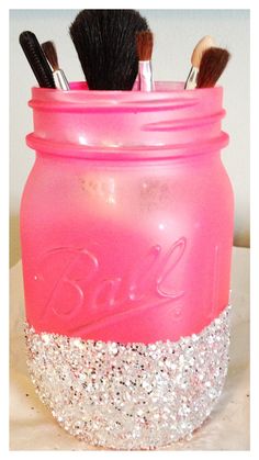 a pink mason jar filled with lots of makeup brushes and some glitter on the lid