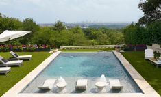 an outdoor swimming pool with lounge chairs and umbrellas on the grass next to it