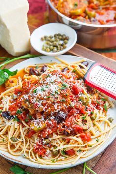 a white plate topped with pasta and sauce next to a grater on top of a wooden table