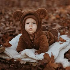 a baby wearing a bear costume laying on a blanket in the middle of some leaves