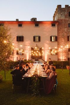 a group of people sitting around a dinner table in front of a building with lights on it