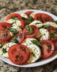 tomatoes, mozzarella and basil on a white plate sitting on a granite counter