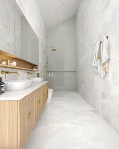 a white bathroom with two sinks and a large mirror over the bathtub, along with gold faucets