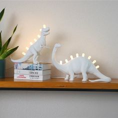 two white dinosaur figurines are on a shelf next to a potted plant