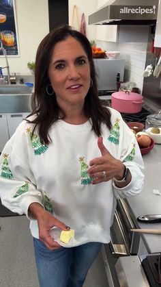 a woman standing in a kitchen holding a piece of food and giving the thumbs up