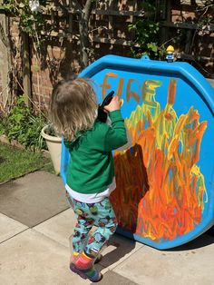 a young child is painting on a large blue box with orange and yellow letters that spell out the word fire