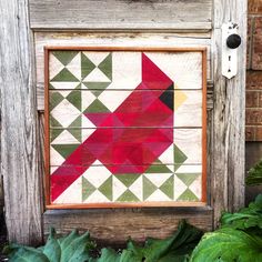 a red bird painted on wooden planks next to green leaves and plants in front of a building