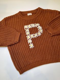 a brown sweater with daisies on it and the letter f is written in white